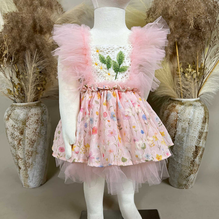 A mannequin displays a pink floral dress with a crochet bodice, green leaf embroidery, and tulle sleeves; the skirt features layered tulle.