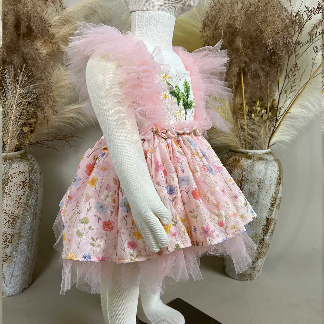 A mannequin a side view of a pink floral dress with a crochet bodice, green leaf embroidery, and tulle sleeves; the skirt features layered tulle