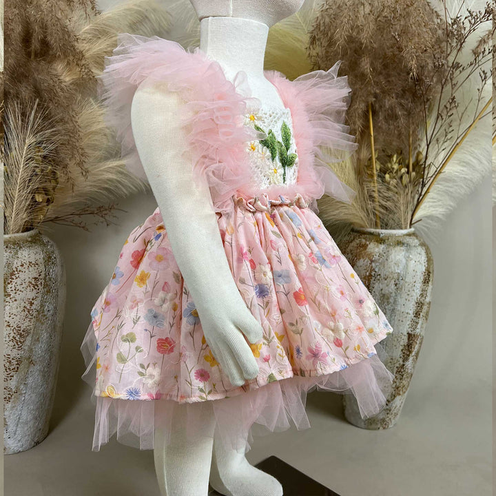 A mannequin a side view of a pink floral dress with a crochet bodice, green leaf embroidery, and tulle sleeves; the skirt features layered tulle