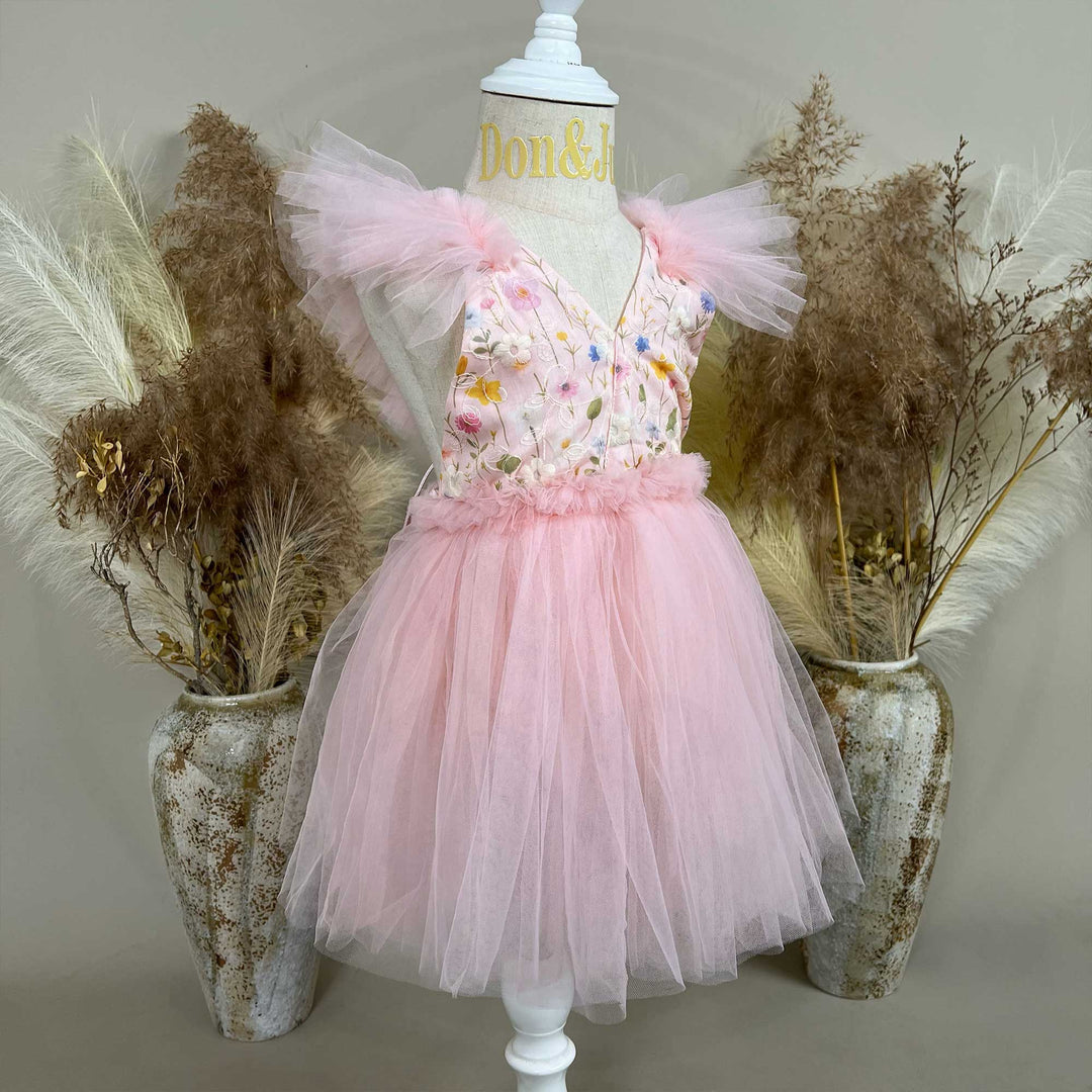 A mannequin a side view of a pink V-neck sleeveless dress with 3D floral embroidery and tulle cap sleeves; the skirt consists of layered pink tulle.