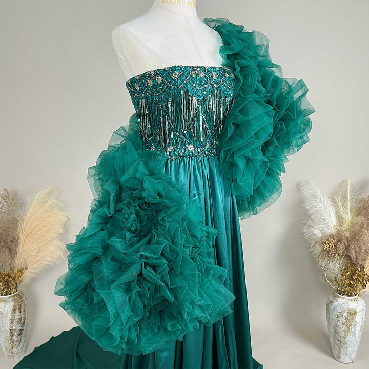 A green one-shoulder evening gown is displayed on a mannequin with beaded details on the bodice.