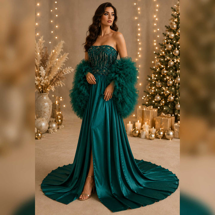 A woman in a green Luna strapless gown and matching feathered shawl stands indoors. A decorated Christmas tree, candles, and gift boxes are visible in the background.
