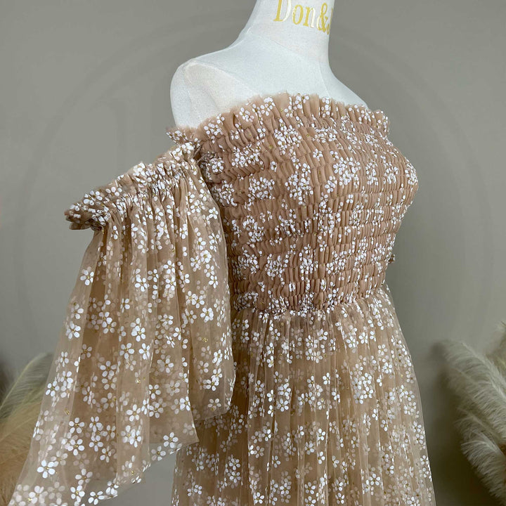 A khaki tulle dress with white floral embroidery and accents is displayed on a white mannequin torso. The dress features a shirred off the shoulder bodice, puffy sleeves details.