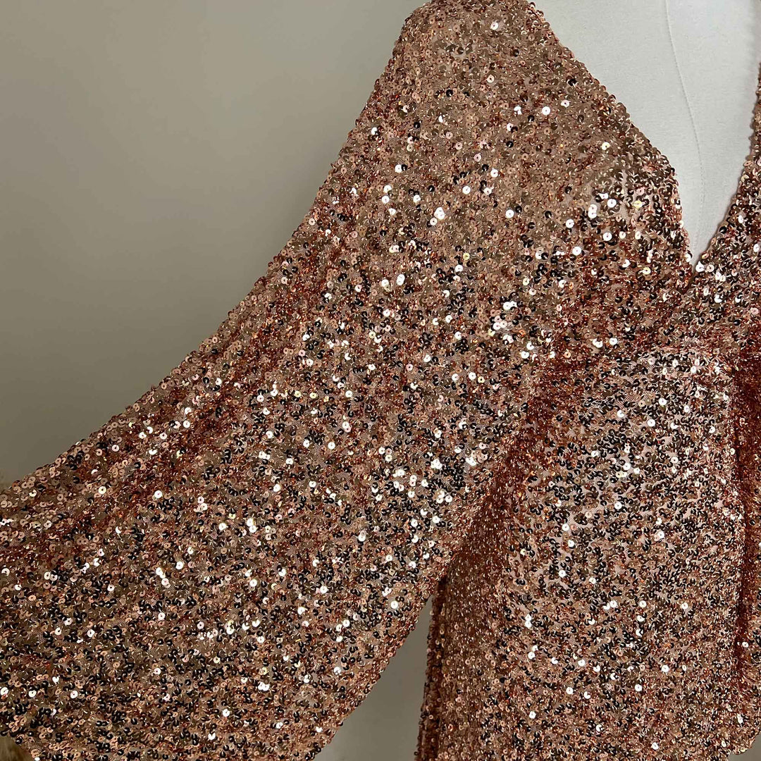 A pink gold Mara dress sequined gown, featuring a V-neck and flared sleeves displayed on a mannequin.