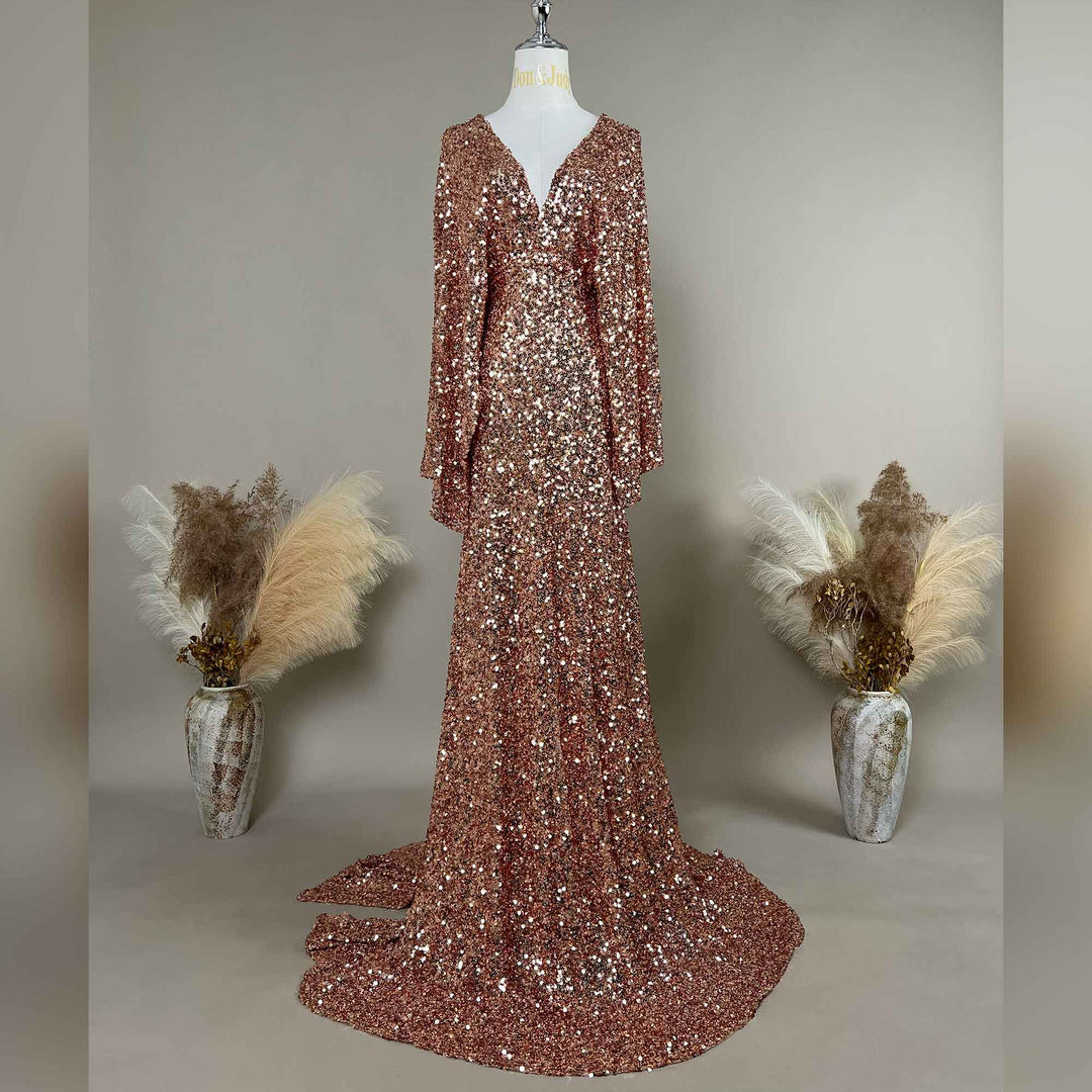 A pink gold Mara sequined gown is displayed on a mannequin, featuring a V-neck and flared sleeves. The hem trails on the floor.
