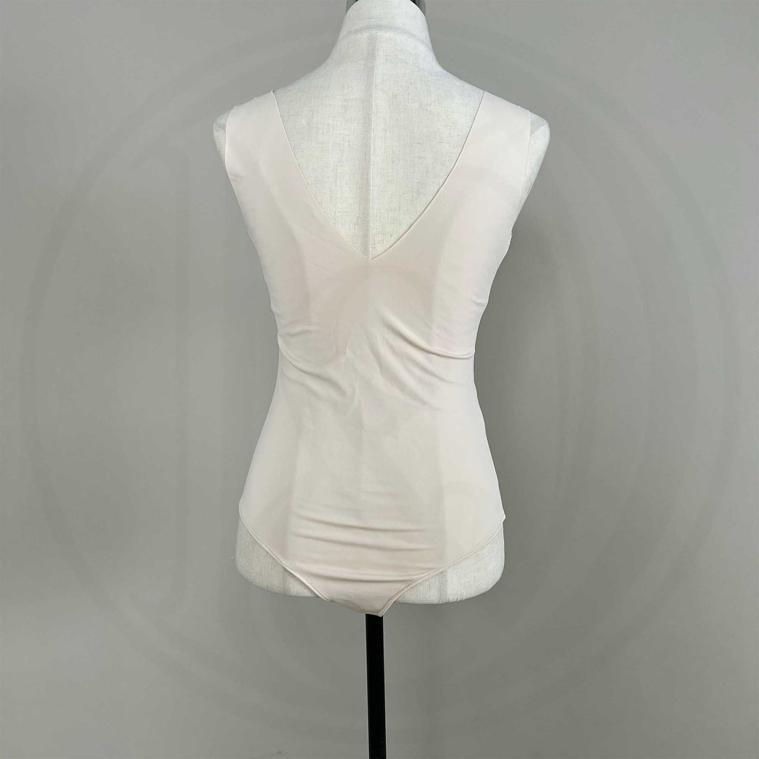 A mannequin shows a back view of a skin sleeveless bodysuit, revealing the V-neck silhouette and fitted cut; the hem features a curved high-cut design.