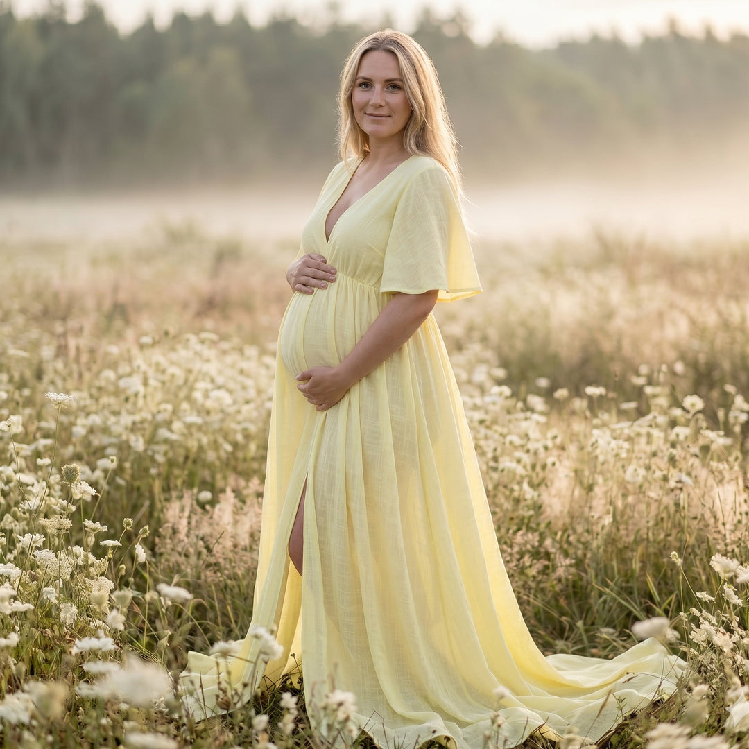 A blonde pregnant woman in a yellow V-neck short-sleeve gown stands holding her belly; the dress features a side slit and train.