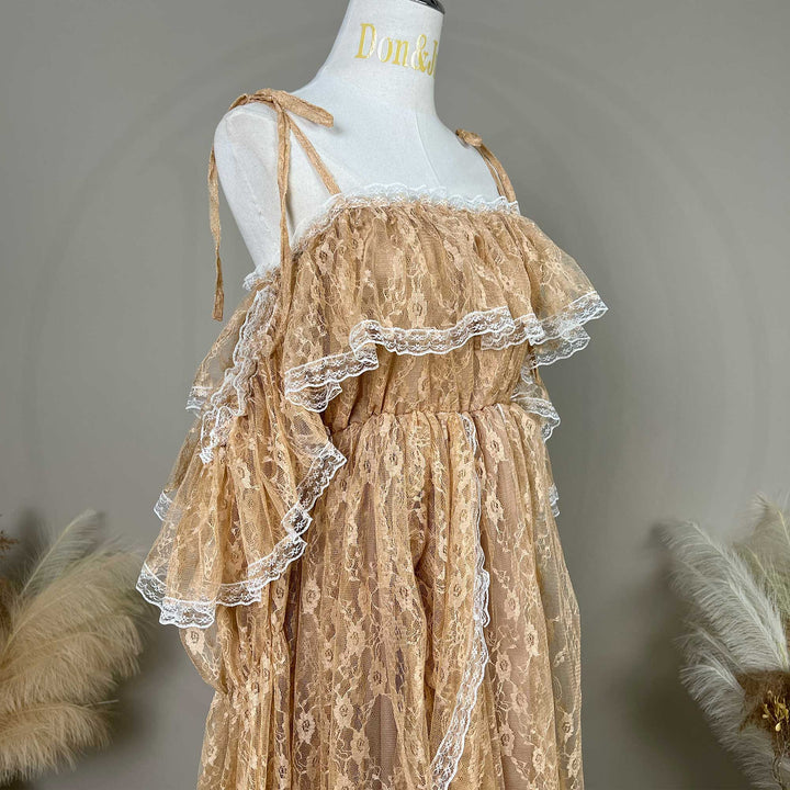A khaki lace maternity dress with dramatic tiered ruffles and off-shoulder sleeves, displayed on a white mannequin torso. The dress features delicate tie-shoulder straps, a gathered elastic waistline, and intricate floral lace fabric trimmed with white scalloped edges.