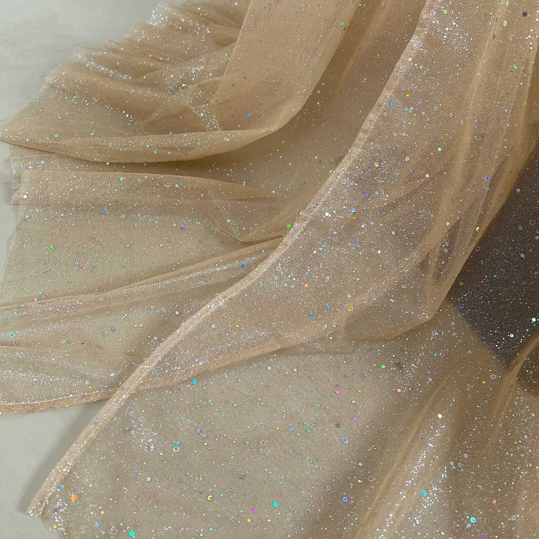 Close-up of champagne tulle fabric with silver and colorful sequins on the surface.