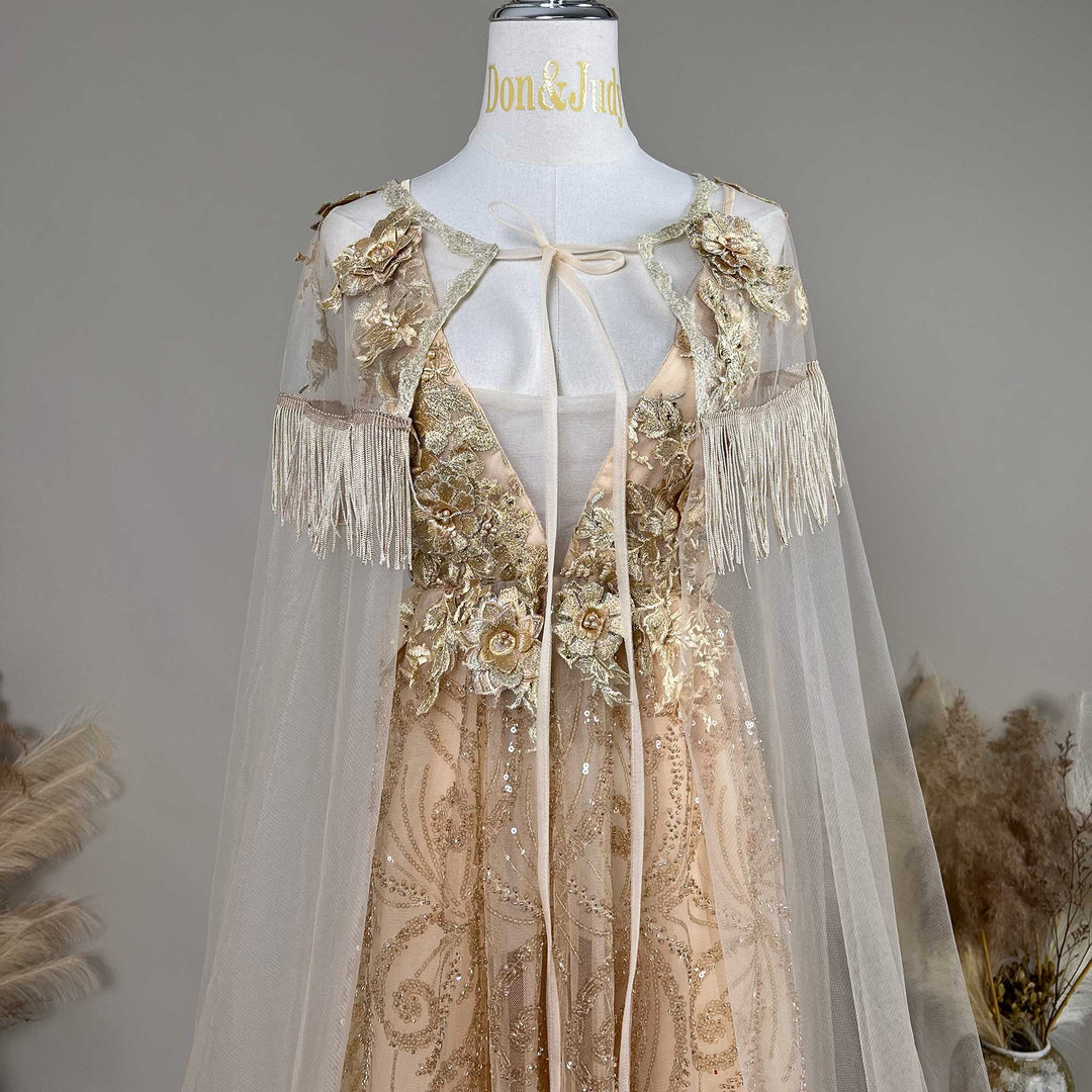 A mannequin displays a gold sequined gown with a tulle cape, featuring 3D floral decorations and fringe cuffs.