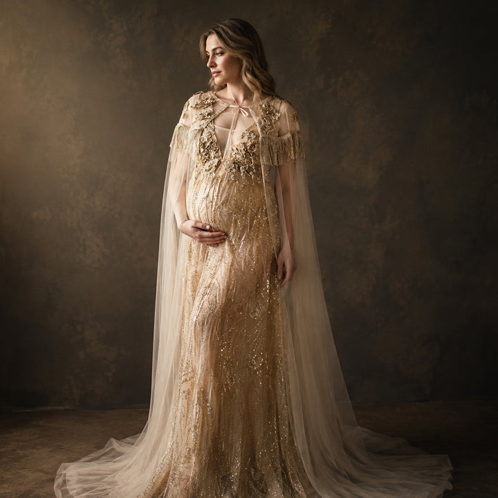 A pregnant model displays a gold sequined gown with a tulle cape, featuring 3D floral decorations and a train skirt.