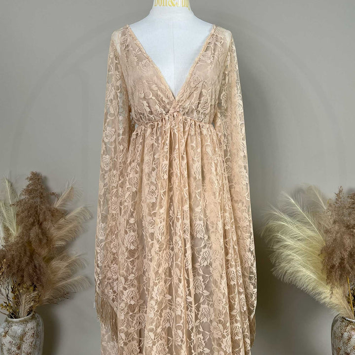 Close up of A beige lace gown is displayed on a mannequin, featuring rose patterns, a ruched high waistline, and fringe cuffs.