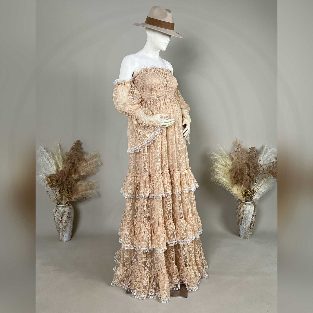 A khaki lace off-shoulder gown is displayed on a mannequin, featuring a shirred bodice, tiered ruffled sleeves, and a multi-layered cake skirt.