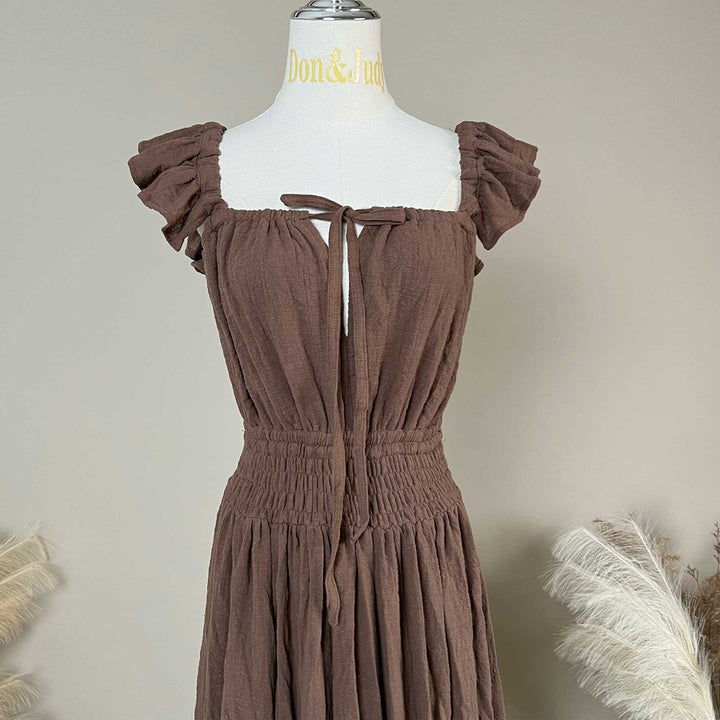 A coffee Tethys gown is displayed on a mannequin,featuring ruffled short sleeves, a front tie, and an elasticated waist.