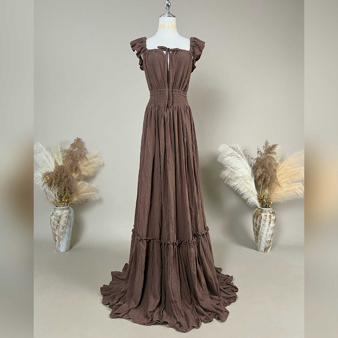 A coffee Tethys gown is displayed on a mannequin with ruffled short sleeves, a front tie, and an elasticated waist; it features a tiered ruffled hem with a train. 