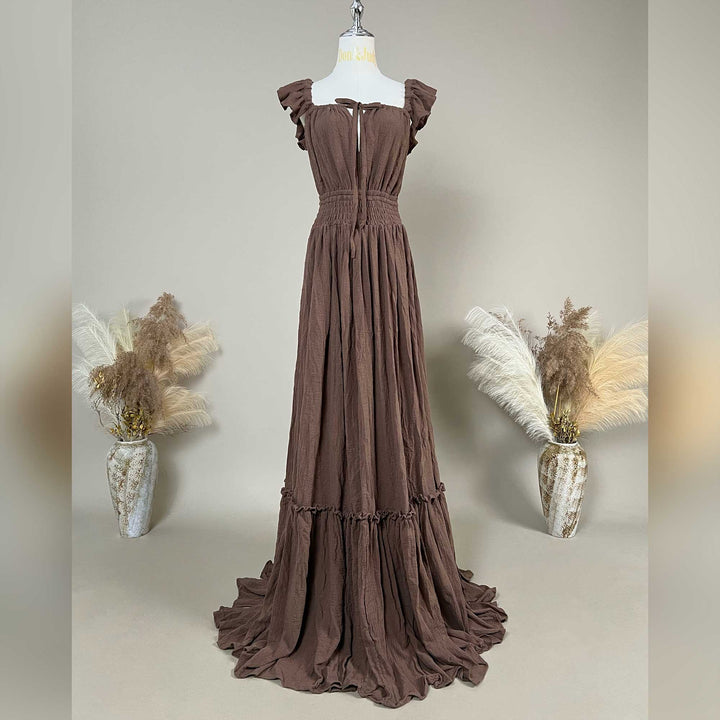 A coffee Tethys gown is displayed on a mannequin with ruffled short sleeves, a front tie, and an elasticated waist; it features a tiered ruffled hem with a train. 