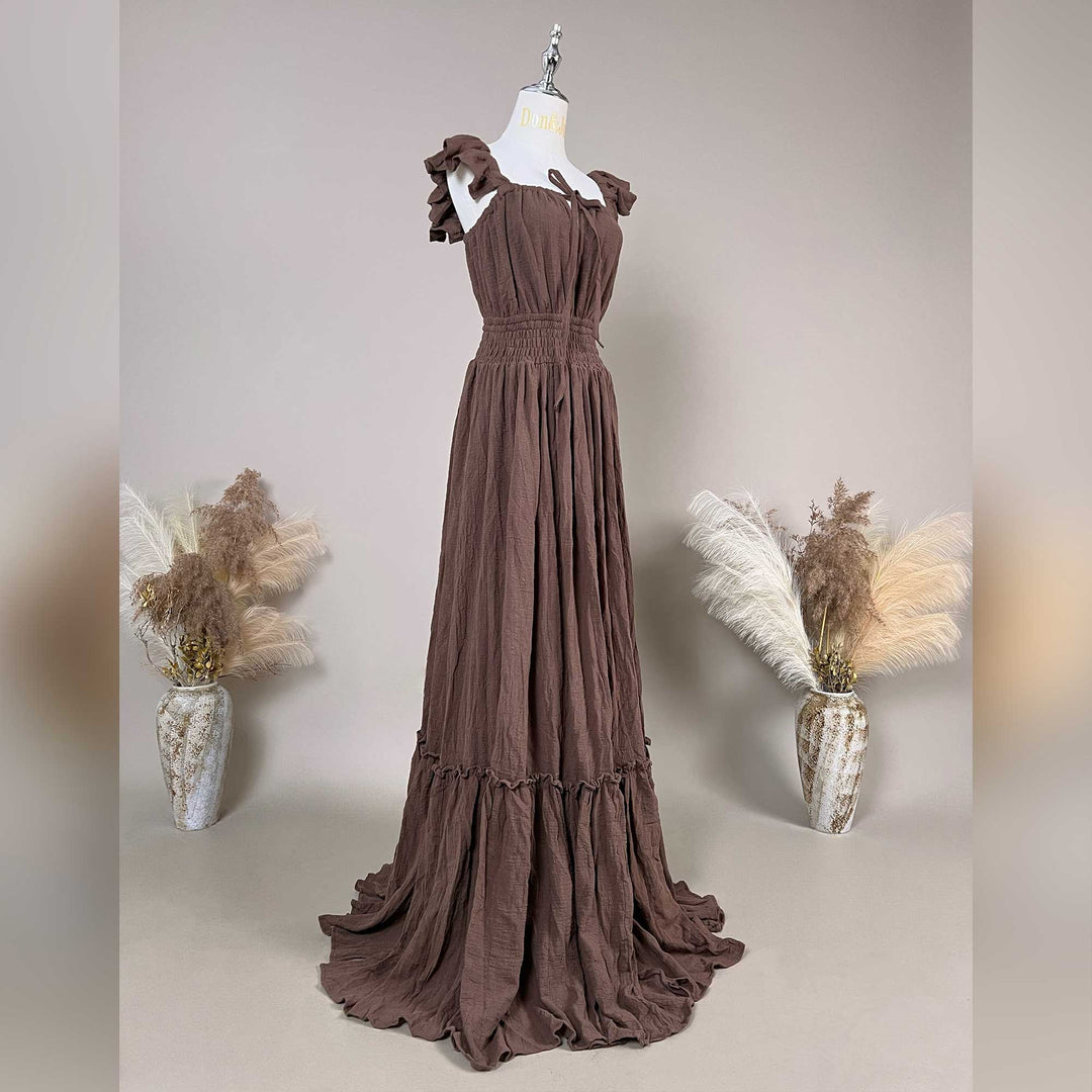 A coffee Tethys gown is displayed on a mannequin, featuring ruffled short sleeves, a front tie, elasticated waist, tiered ruffled hem, and train.