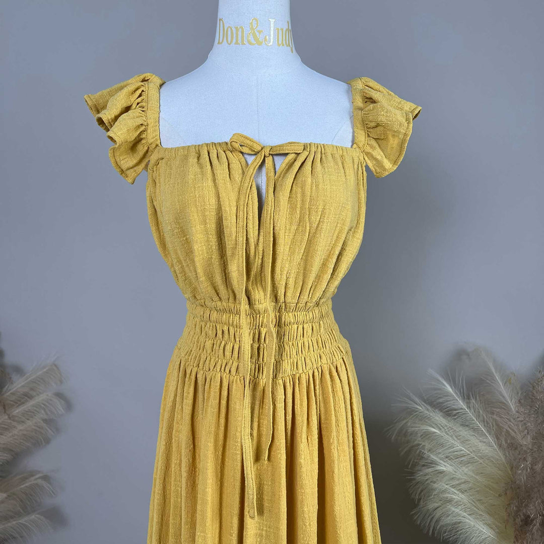 A Tethys gown is displayed on a mannequin,featuring ruffled short sleeves, a front tie, and an elasticated waist.