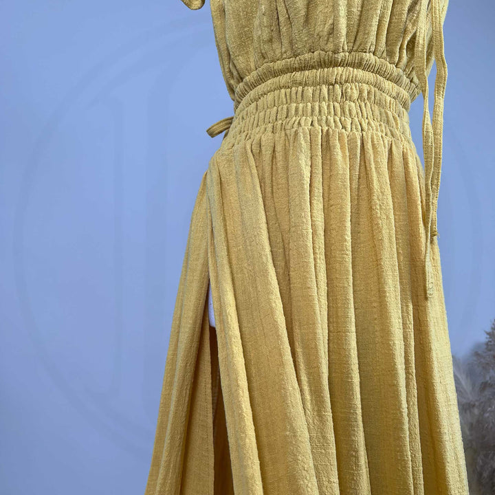 A close-up of a Tethys gown on a mannequin shows a wide elasticated shirred waist, hanging ties, and a side slit in textured fabric.
