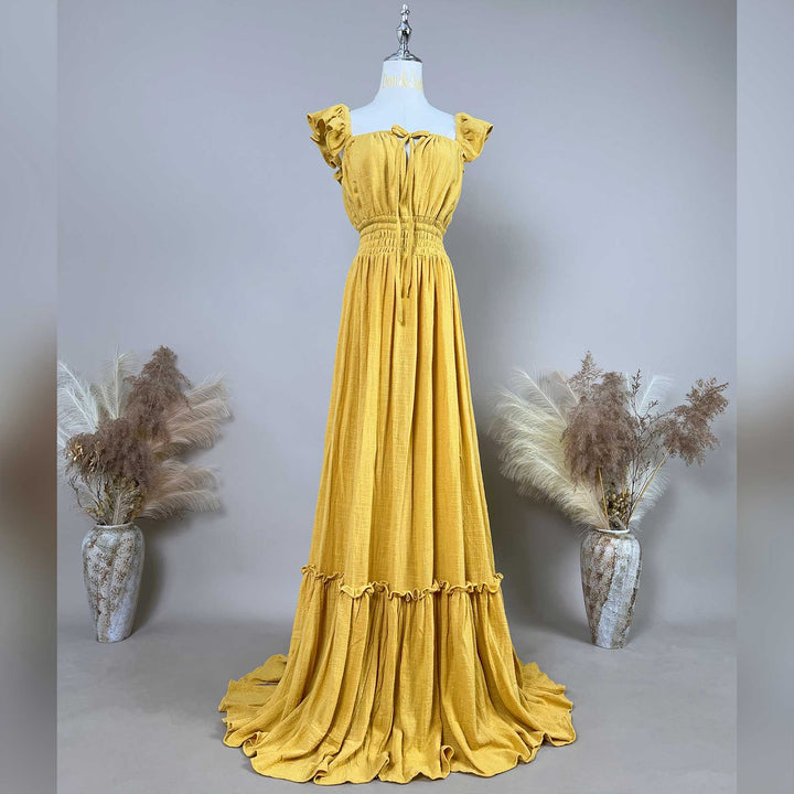 A yellow gown is displayed on a mannequin with ruffled short sleeves, a front tie, and an elasticated waist; it features a tiered ruffled hem with a train. 