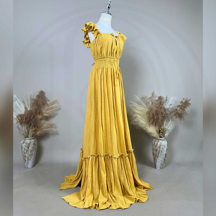 A Tethys gown is displayed on a  mannequin, featuring ruffled short sleeves, a front tie, elasticated waist, tiered ruffled hem, and train.