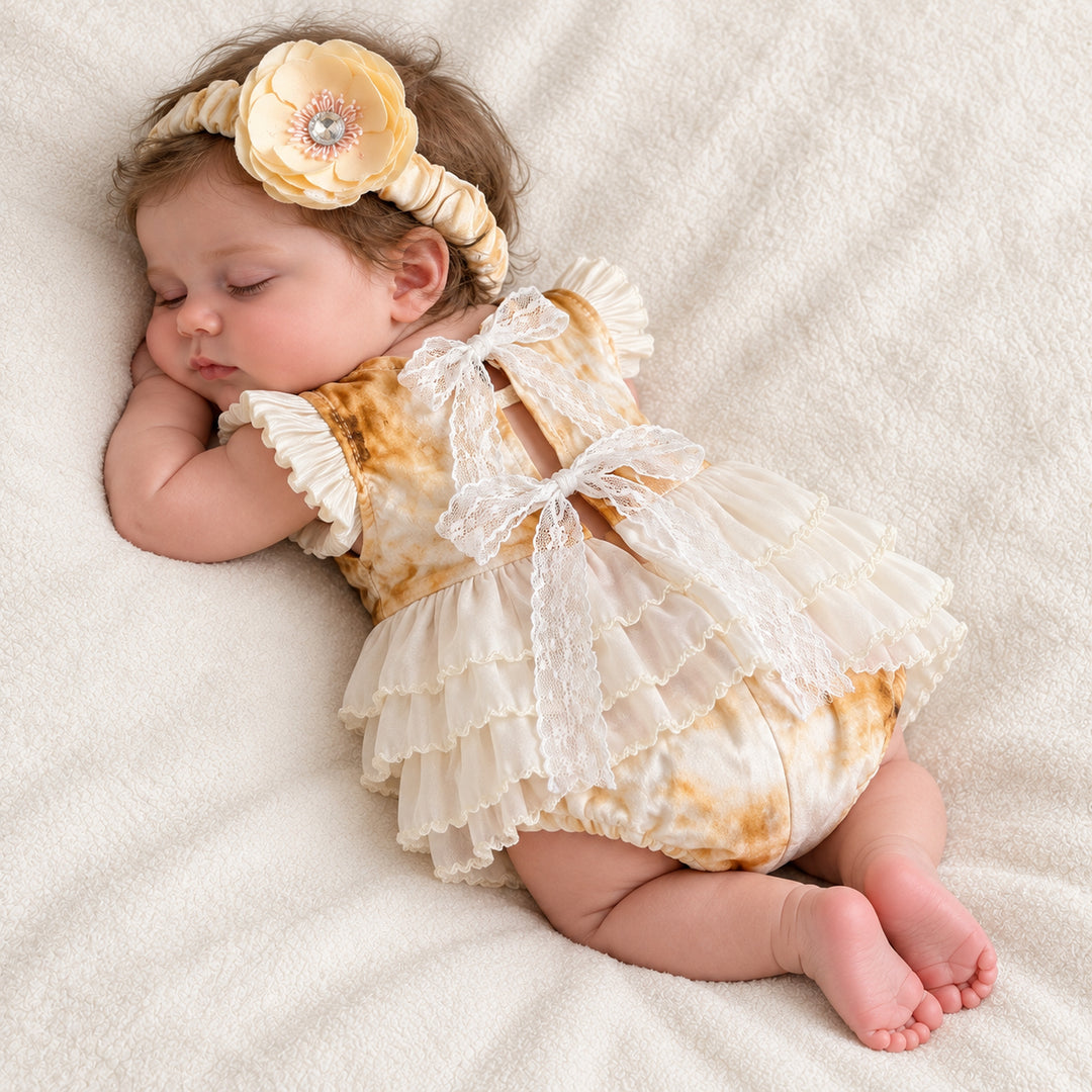 A baby lying on her side, showing the lace ribbon bow on the back and the tiered skirt, head resting on her arm.