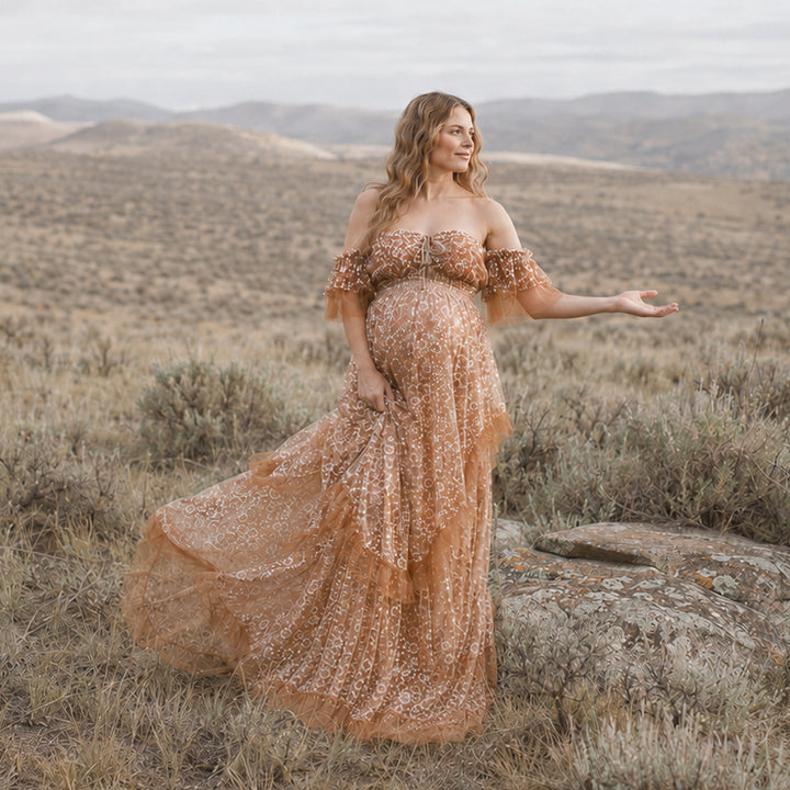 The woman is wearing Khaki Tyche stands outdoors; she extends her left hand and lifts the skirt with her right, with hills and dry vegetation in the background.
