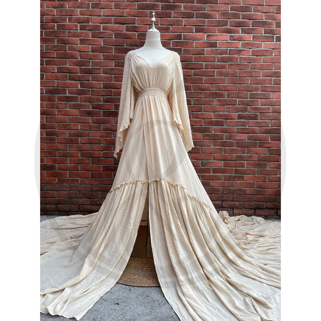 A Daphne ivory long-sleeved V-neck gown is displayed on a mannequin, with hands positioned on the simulated belly. The dress features a high front slit and its hem and train are spread out on the wooden floor.